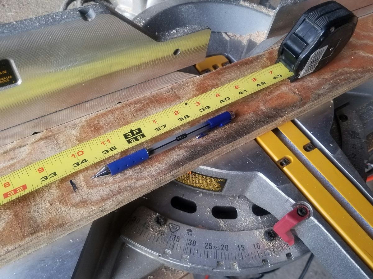 Tape measure and pencil resting on a length of trim at a miter saw.
