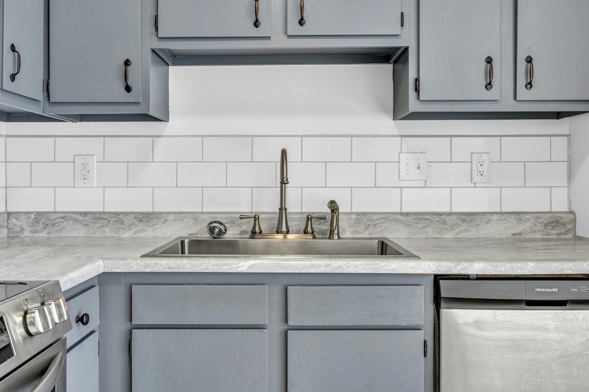 Gray painted kitchen cabinets with dark pulls around a sink and white tile backsplash.