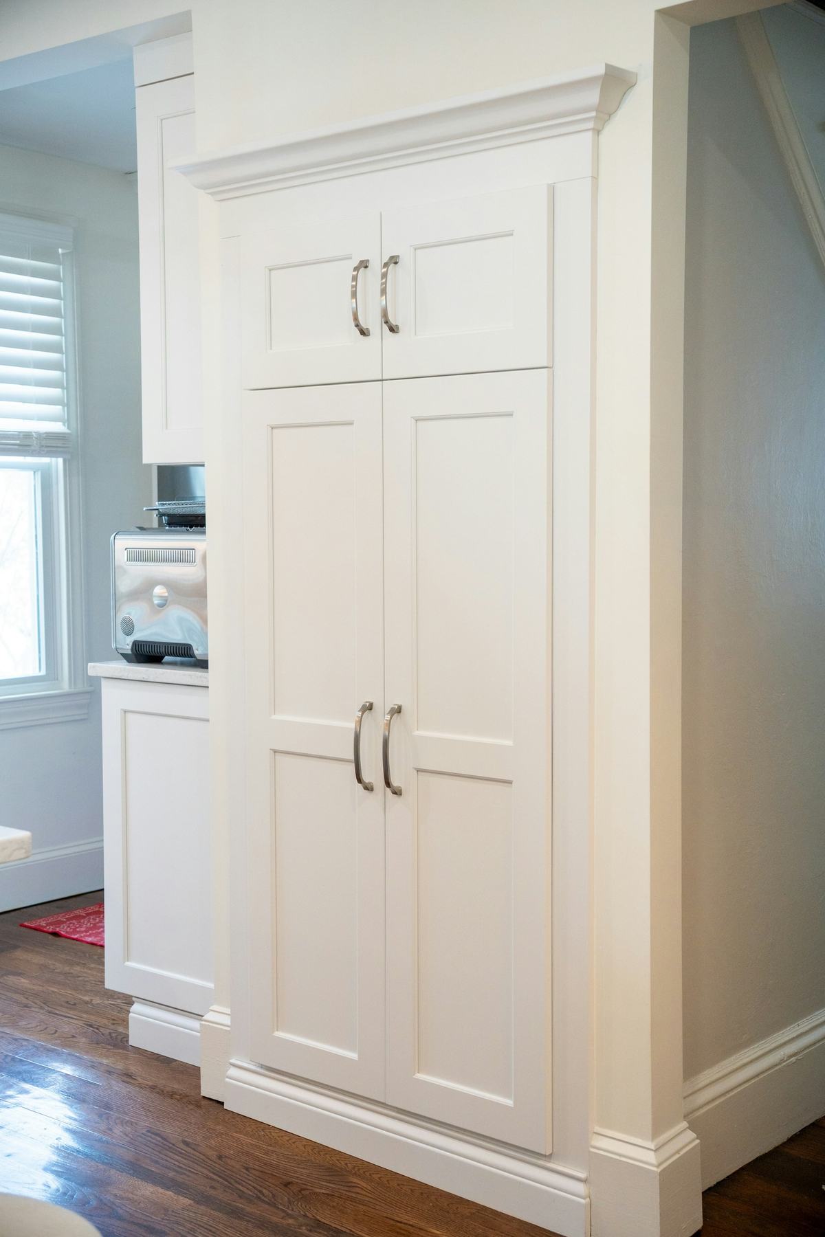 Tall white pantry cabinet with paneled doors in a kitchen.
