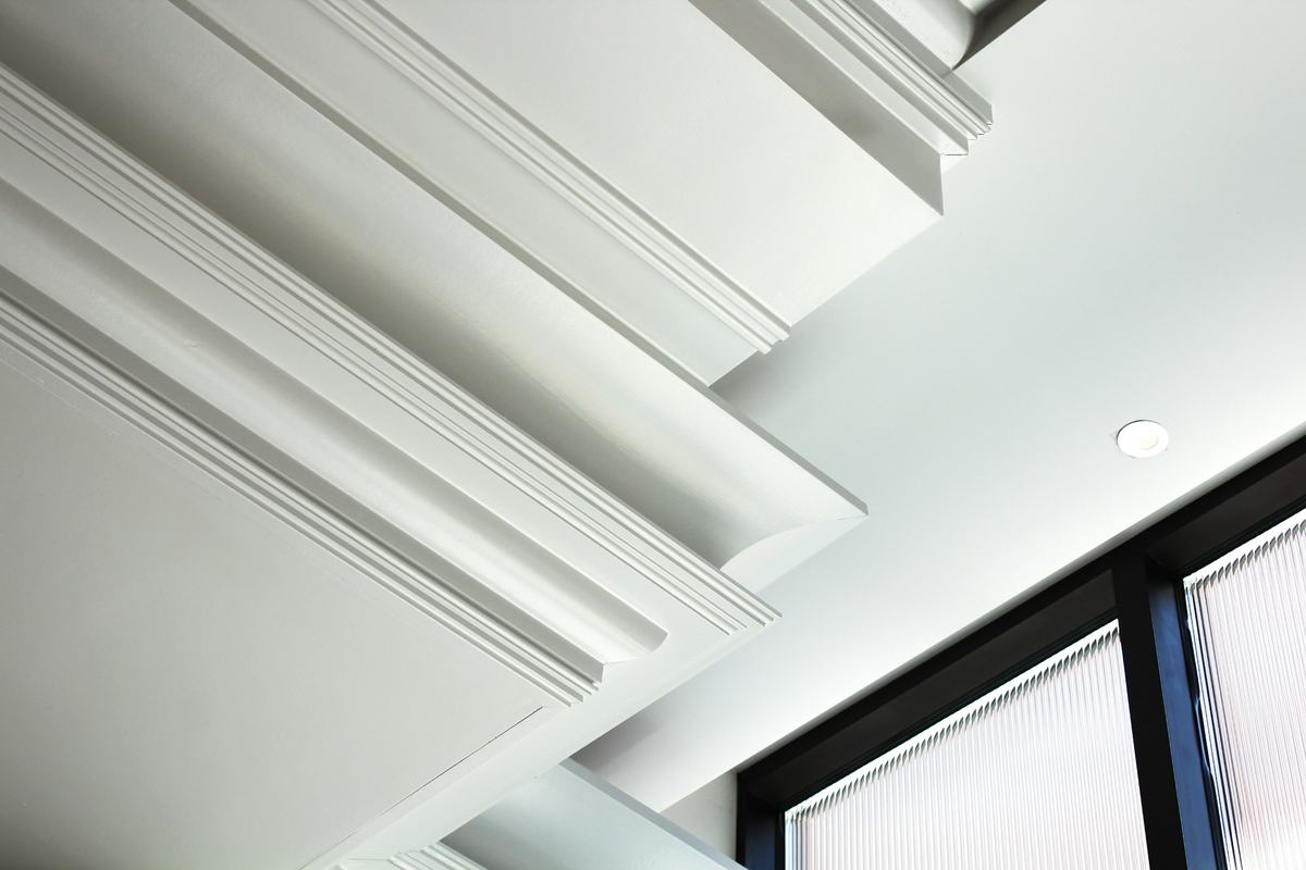 White coffered ceiling with layered crown molding and a recessed light, seen from below.