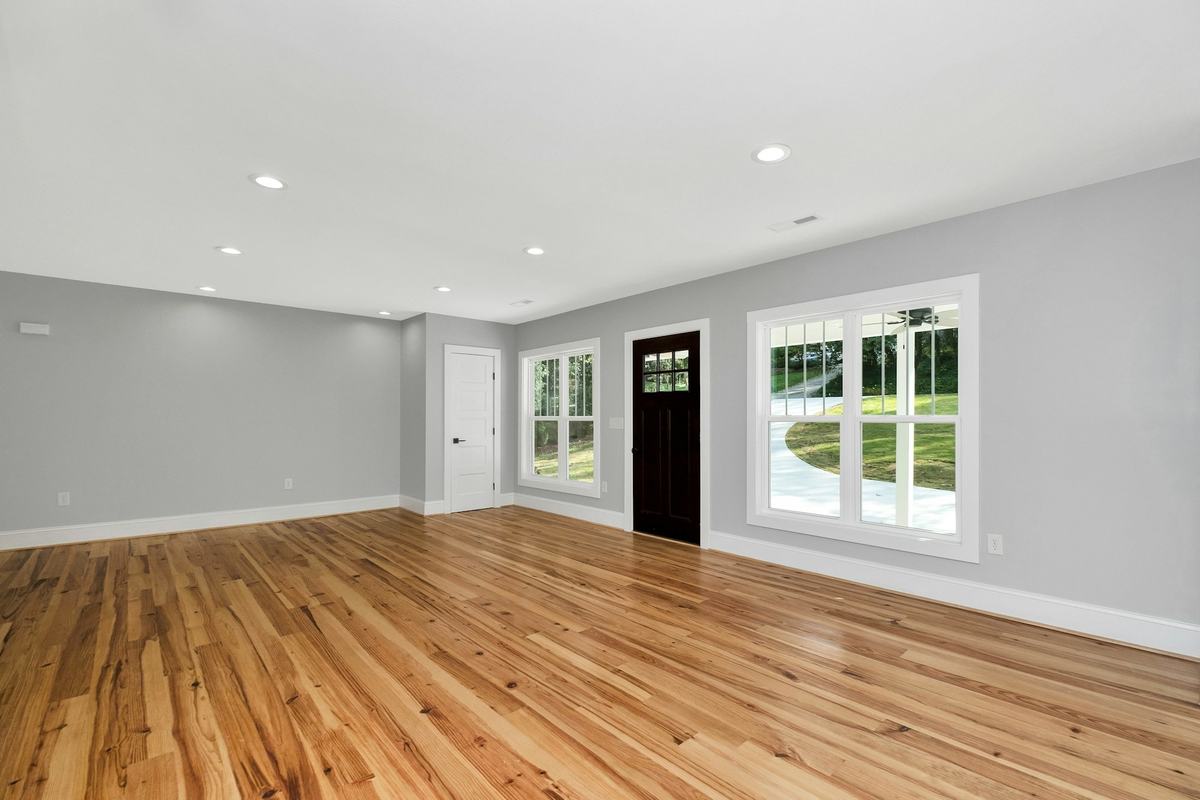 Empty living room with gray walls, white trim and wood flooring.