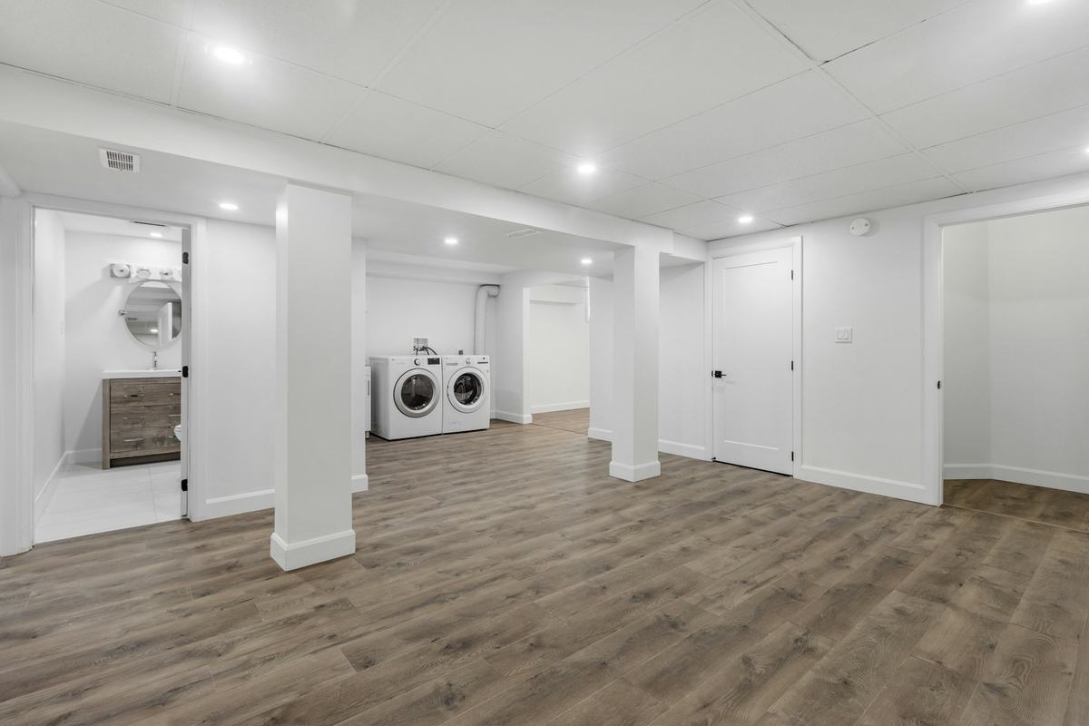 Finished lower-level interior with white painted walls, white doors and baseboards, recessed lighting and wood-look plank flooring.