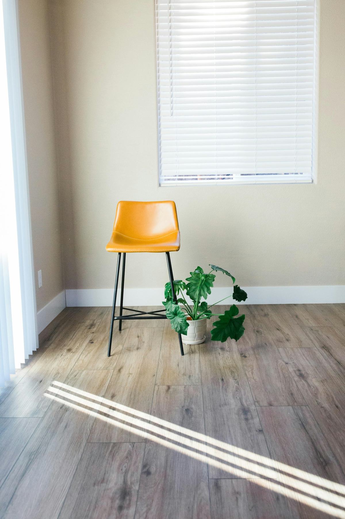 Corner of a room with wood-look plank flooring meeting a white baseboard under a window.