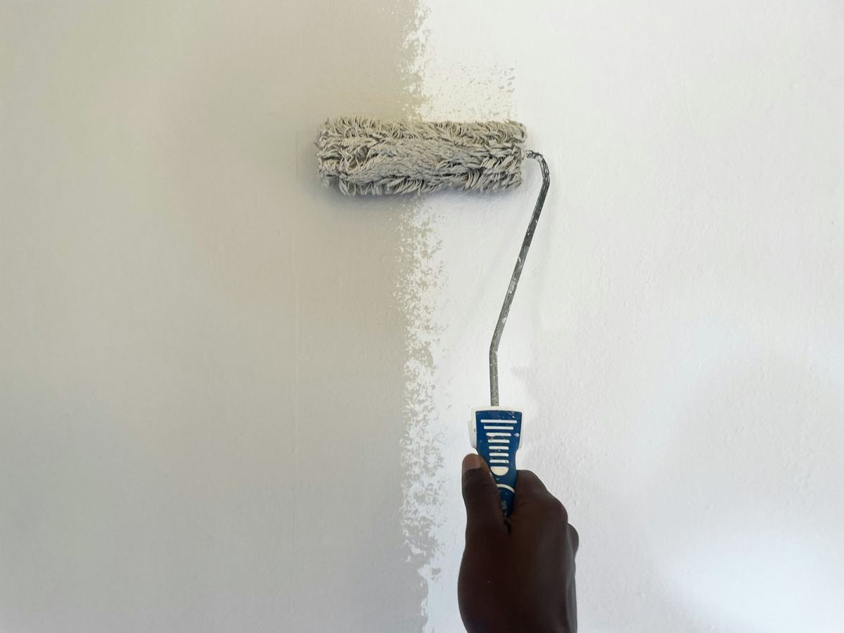 Hand rolling white paint onto an interior wall with a nap roller.