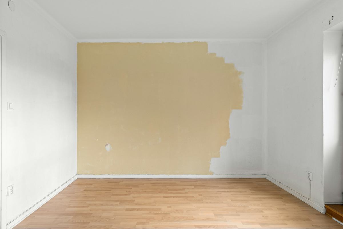Empty room with one wall partly rolled in a new color over the previous white.