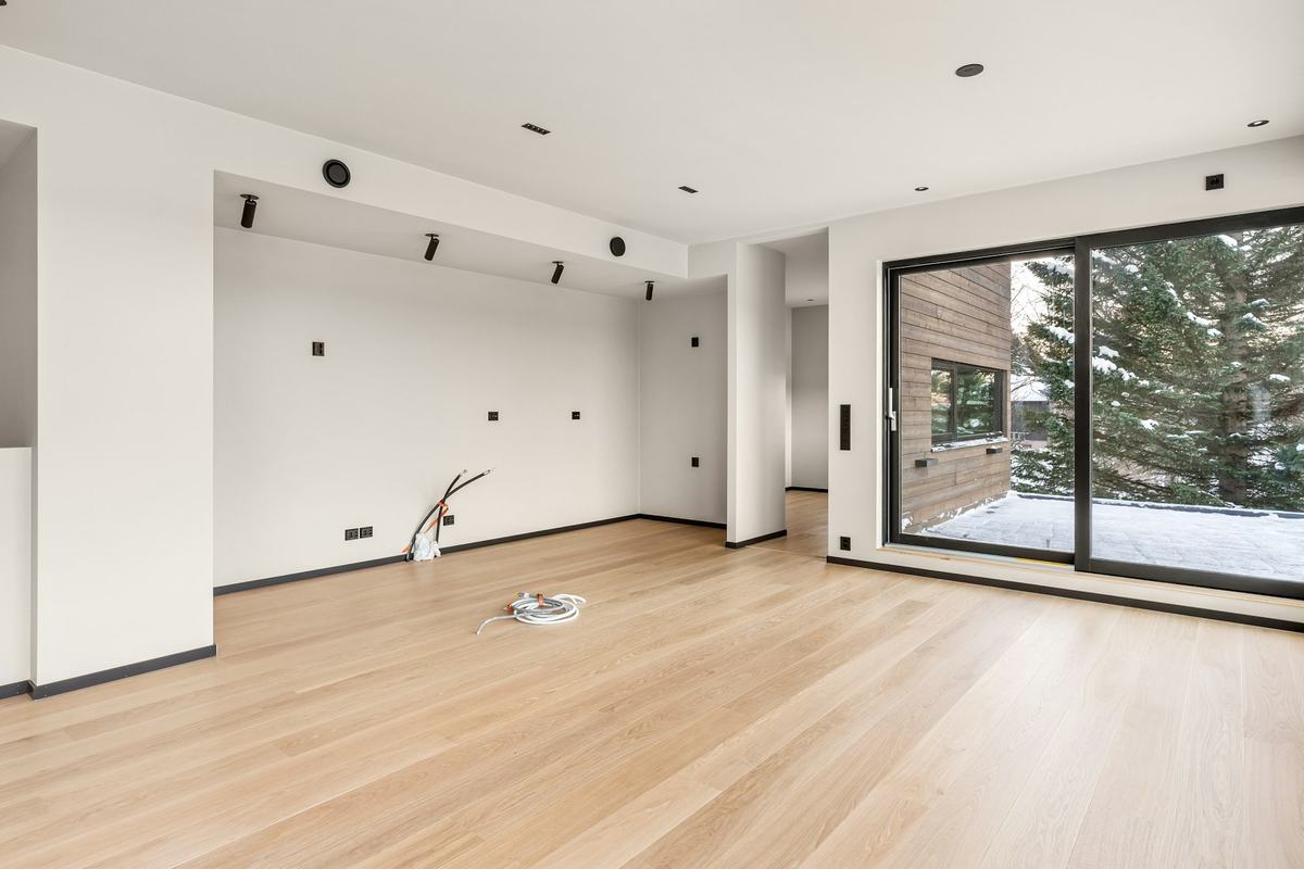 Empty finished room with white walls, light wood flooring and large glass doors.