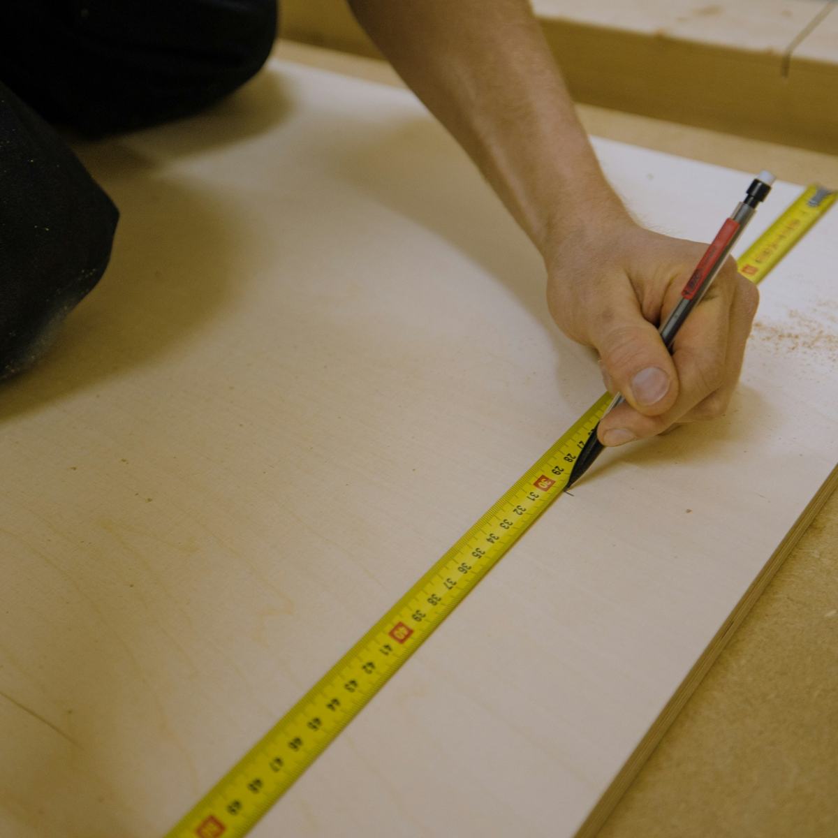 Hand marking a board with a pencil against a tape measure.
