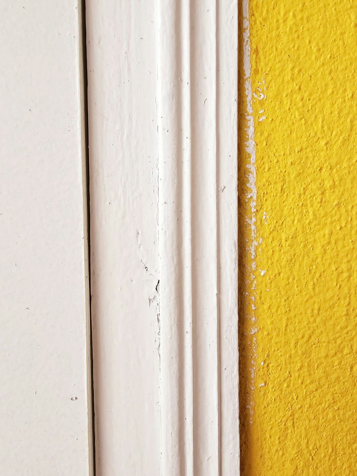 Close view of white painted door casing profiles next to a yellow textured wall.